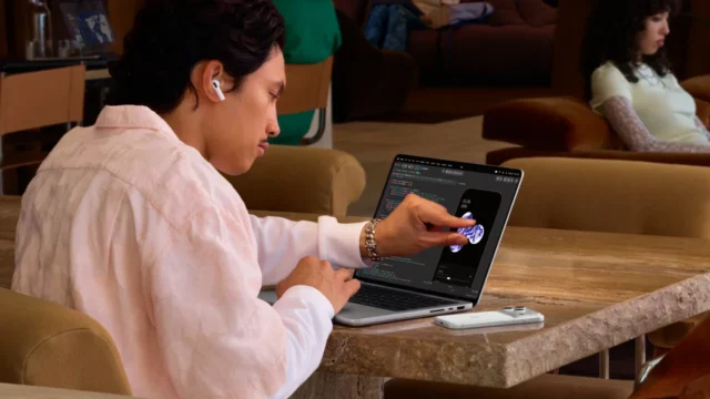 dokunmatik-macbook-pro-deneyimi-1 Masada açık duran bir dizüstü bilgisayarın ekranına parmakla dokunan kullanıcı
